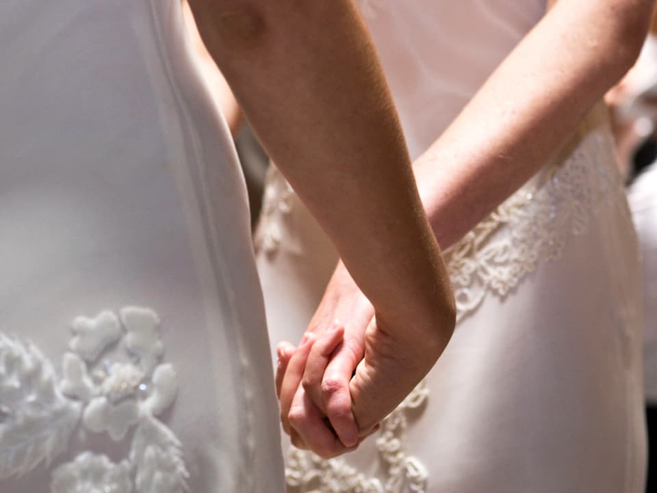 Die Hände von zwei weiss gekleideten Frauen, die sich halten.