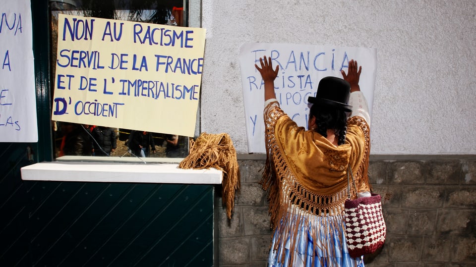 Eine Bolivianerin protestiert in La Paz und klebt Poster an die französische Botschaft.
