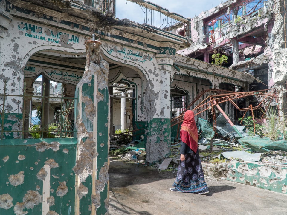 Eine Frau betritt eine zerstörte Moschee