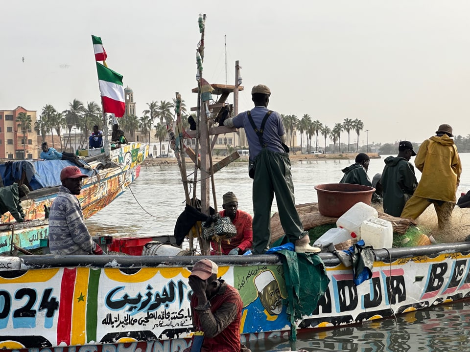 Mehrere Personen stehen auf einem farbig bemalten Boot im Hafen