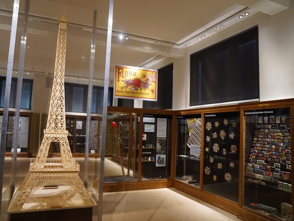 Links im Bild steht eine Miniaturversion des Eiffelturms, aus feinen Zündhölzern gebaut, daneben sieht man Vitrinen.