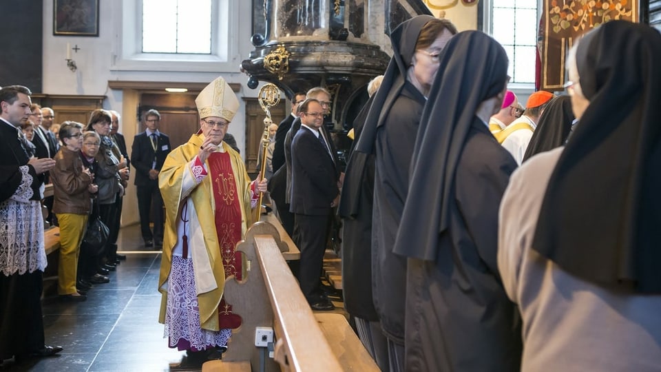 Ein Bischof in einer vollen Kirche, er blickt in die Kamera.