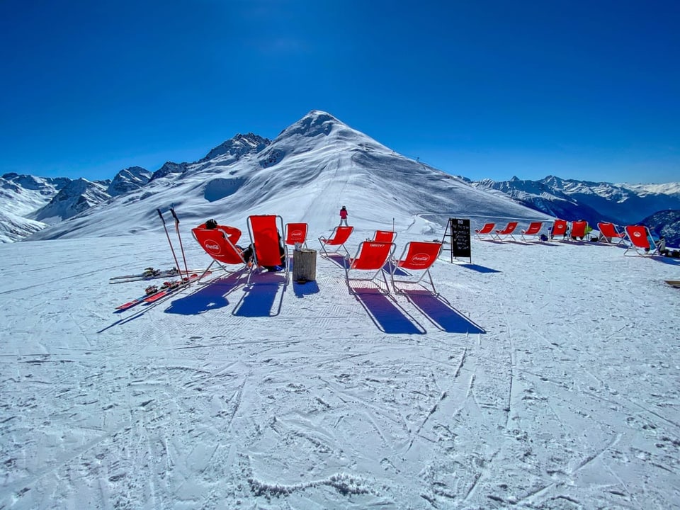 Liegestühle im Schnee bei strahlend blauem Himmel.