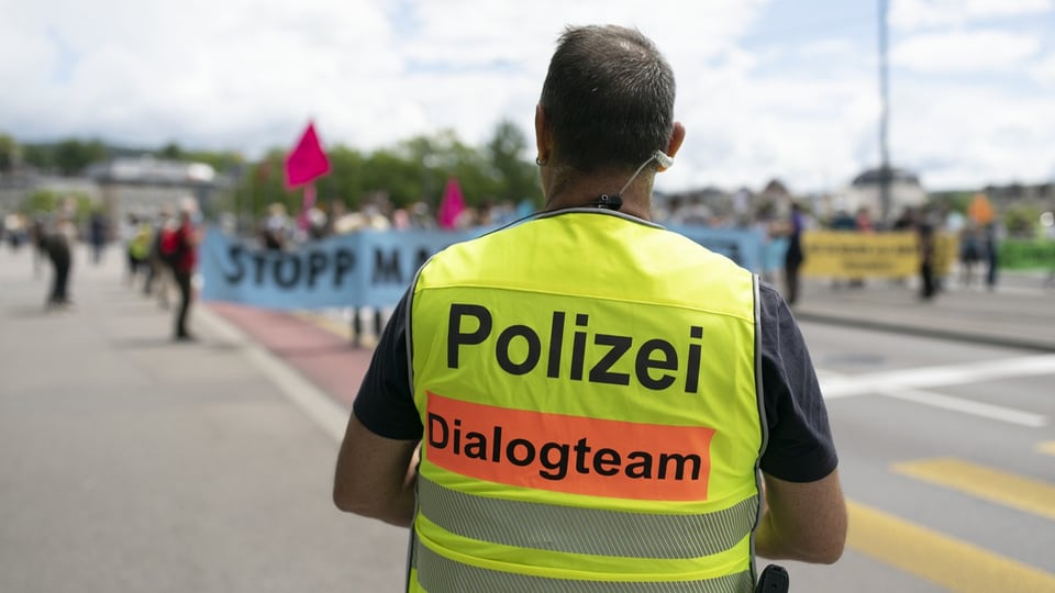 Blick von hinterem einem in einer gelben Schutzweste gekleideten Polizisten auf einen Demonstrationszug