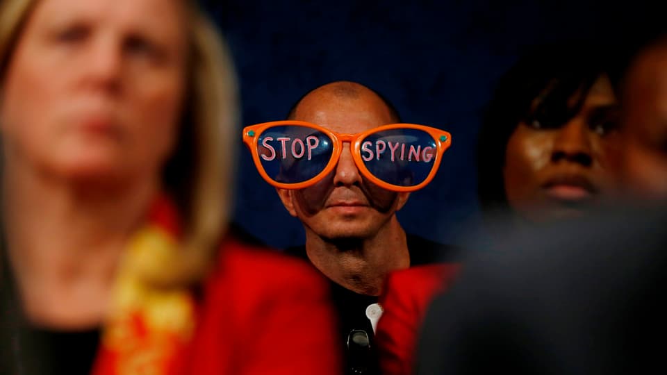 Ein Zuschauer sitzt während einer politischen Anhörung im Publikum mit einer auffällig grossen Brille mit den Worten «Stop Spying».