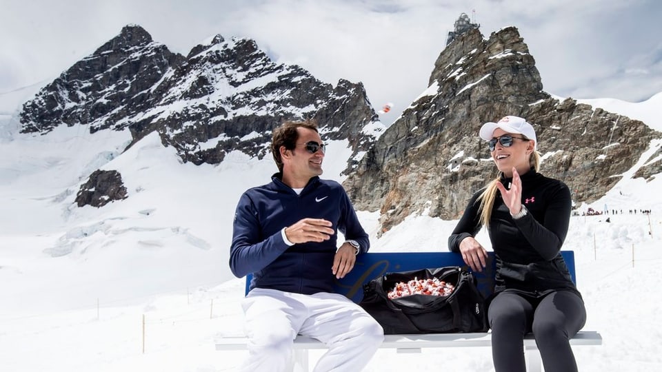 Roger Federer und Lindsey Vonn sitzuen auf einer Bank auf dem Jungfraujoch, zwischen ihnen eine Tasche voller Lindt-Schoggi.