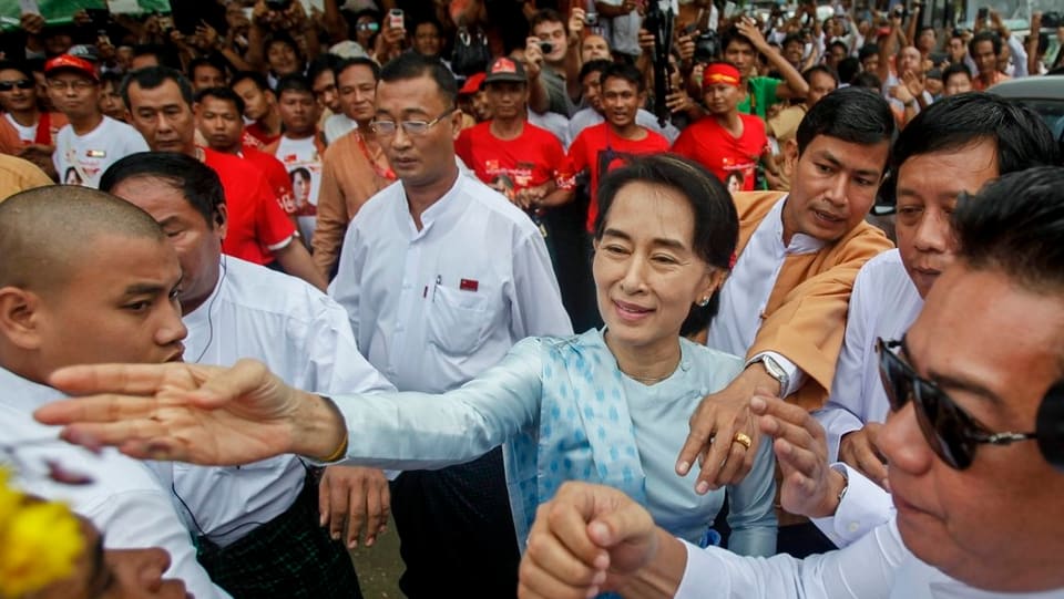 Aung San Suu Kyi in einer Menschenmenge. Sie nimmt Blumen eines Anhängers entgegen.