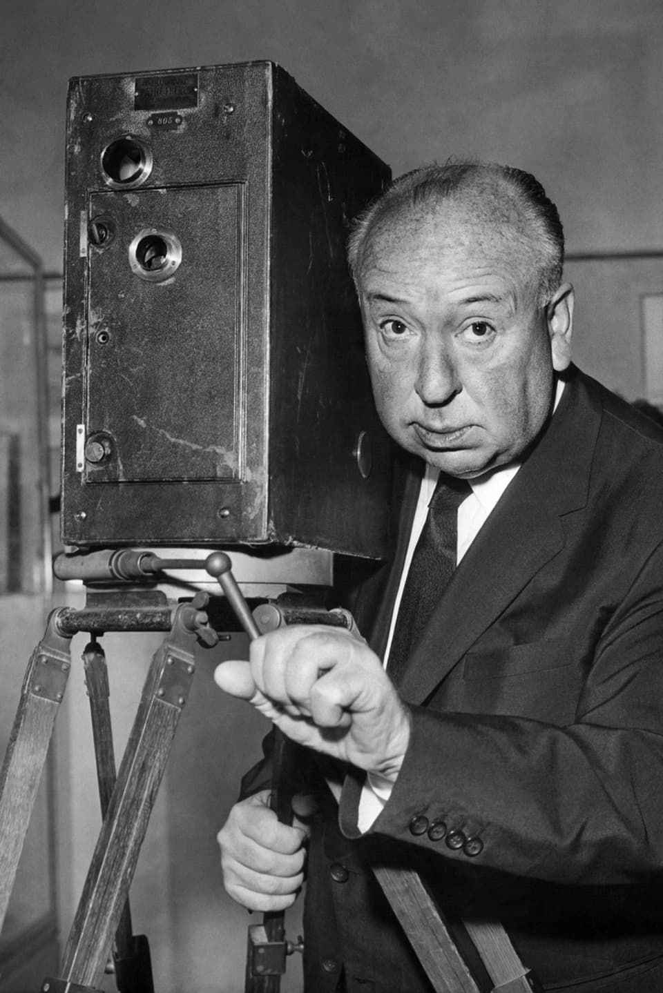 Alfred Hitchcock posiert hinter einem alten Projektionsgerät.