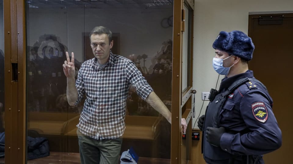 Nawalny steht in einem Glaskäfig. Ein Polizist steht daneben. 
