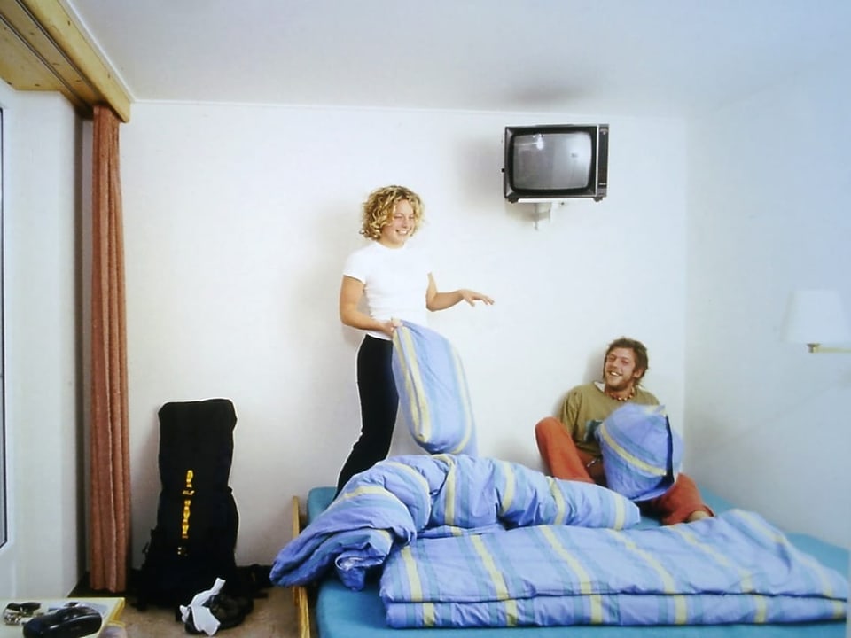 Frau und Mann spielen mit Kissen auf einem Bett in einem hellen Zimmer.