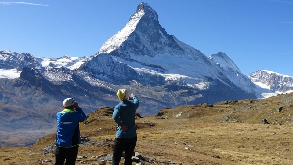 Zwei Wanderer vor dem weissen Matterhorn.