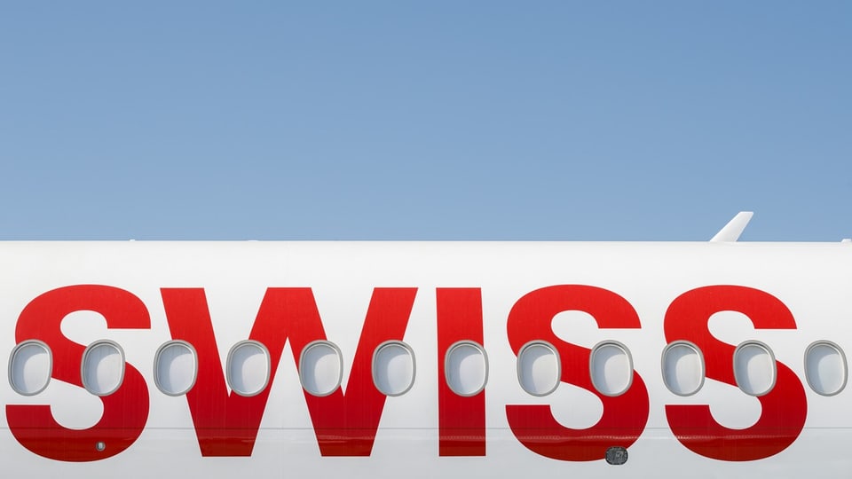 Seitenansicht eines Flugzeugs mit dem Schriftzug 'SWISS' und Fensterreihen vor einem blauen Himmel.