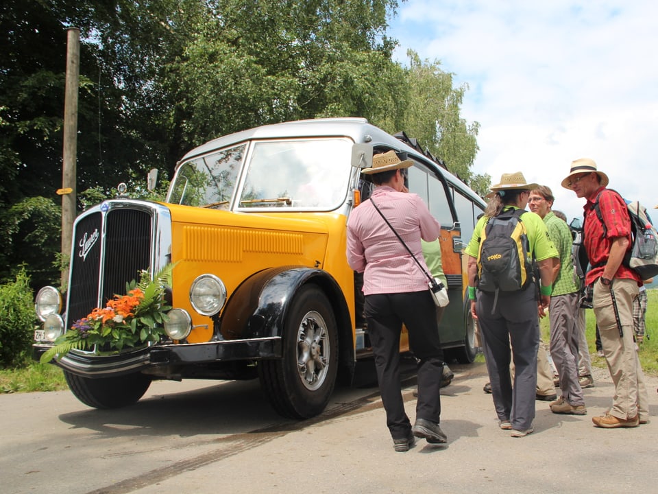 Vor einem mit Blumen geschmückten Oldtimer-Postauto stehen ein paar Wanderinnen und Wanderer.