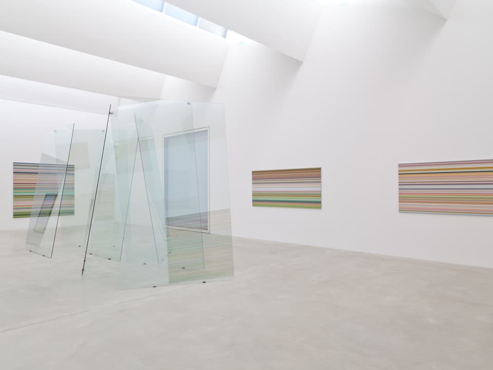 Ein Raum it Glasscheiben in der Mitte und Bildern mit farbigen Streifen an der Wand.