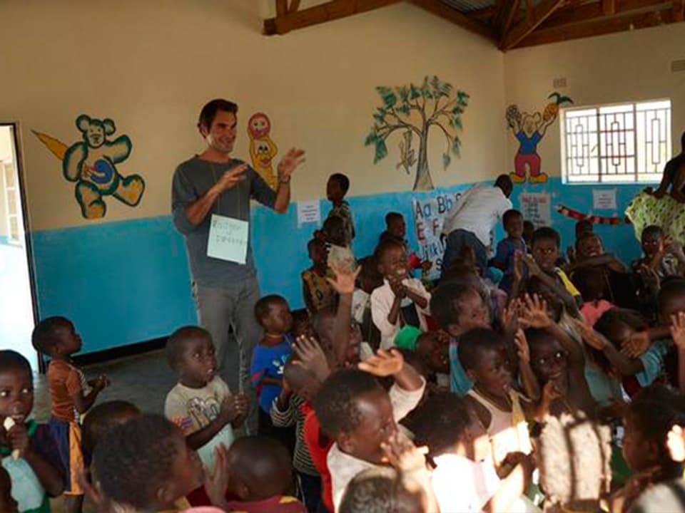 Roger Federe steht in einem Schulzimmer. Um ihn herrum stehen viele, kleine, malawische Kinder. 