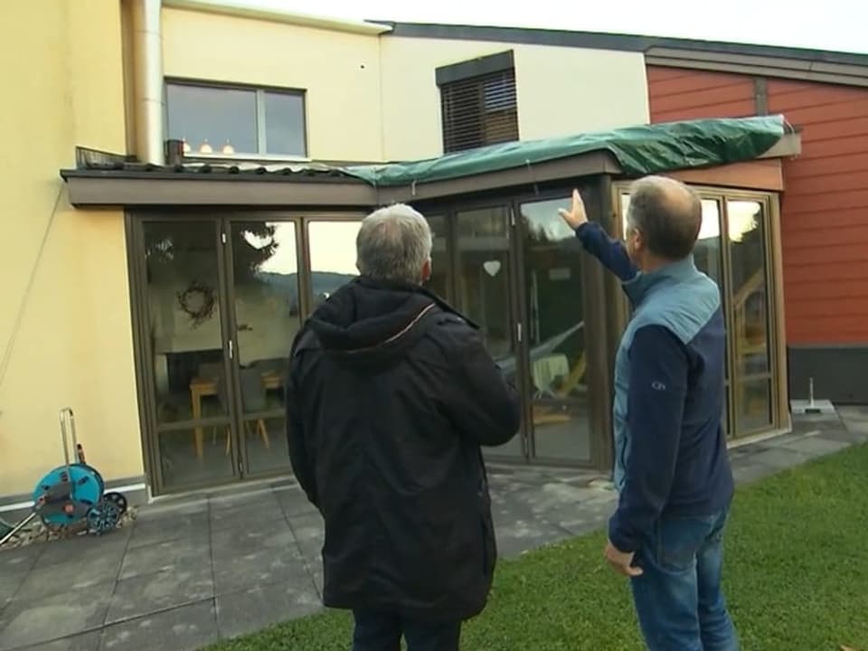 Zwei Männer stehen vor einem beschädigten Dach