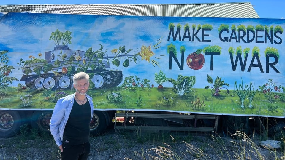 Robert Hall steht vor einem mit dem Schriftzug «Lastwagen im Ecovillage in Visby, Schweden «Make Gardens – not War»