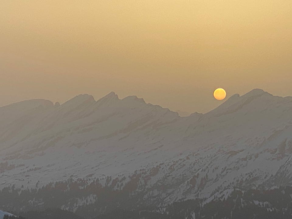 Blick auf Schneebergekrete mit Sonnenscheibe am braunen bis gelben Himmel