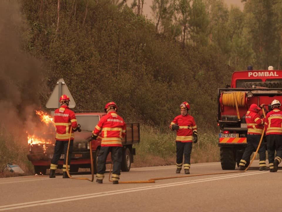 Feuerwehrleute löschen ein brennendes Auto.