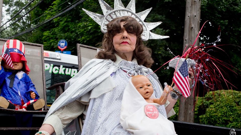 Eine als Freiheitsstatue verkleidete Frau mit Puppe und «Pro-Life»-Batch