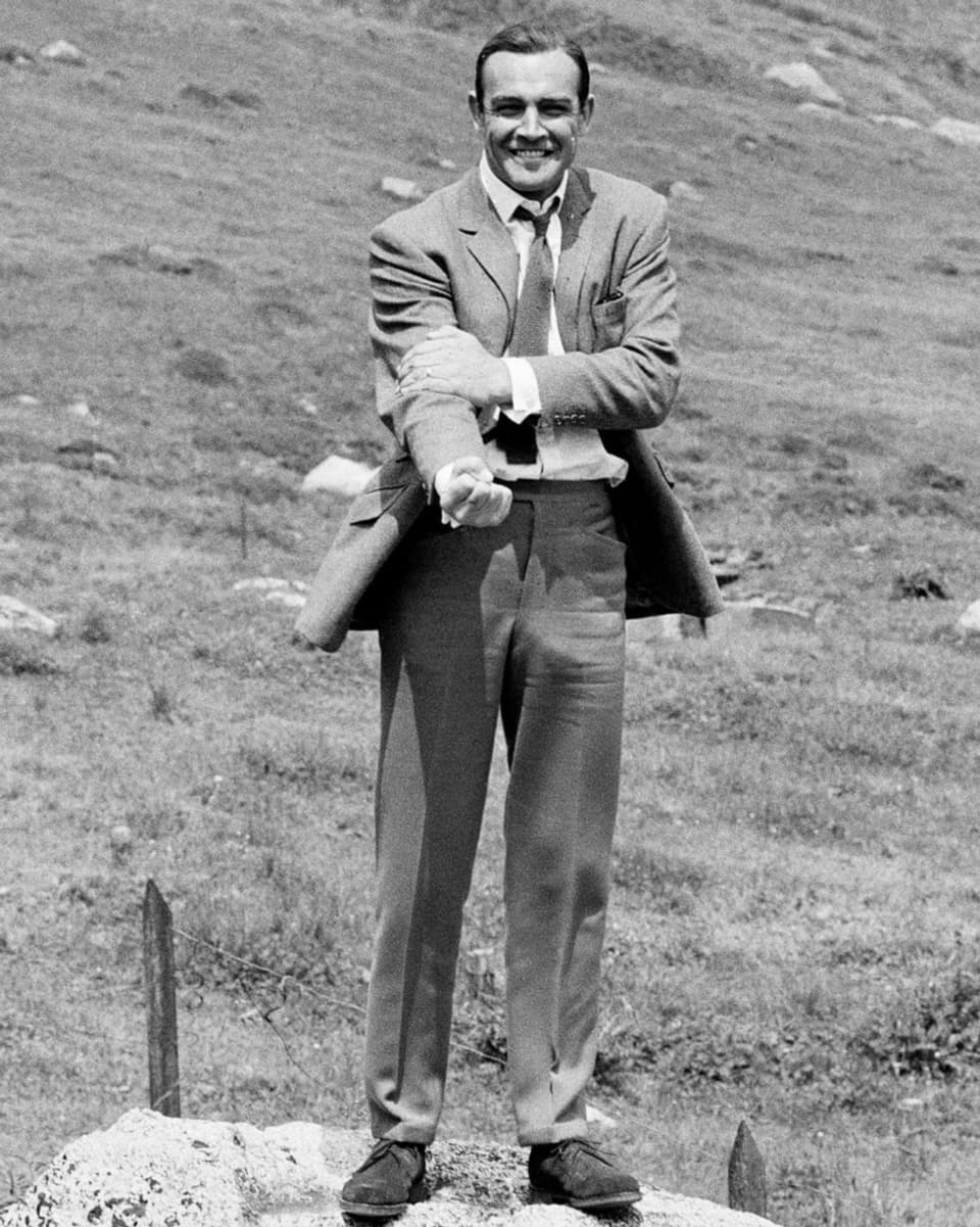schwarz-weiss Foto Mann steht im Anzug auf Stein in den Bergen.