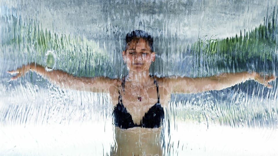 Frau im Bikini steht unter dem Wasserstrahls eines Brunnens