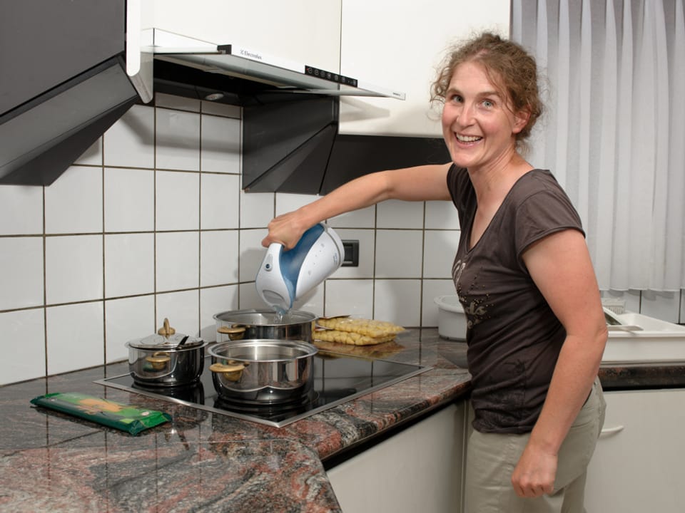 Katia Ambrosini steht in ihrer Küche am Herd und giesst heisses Wasser aus dem Wasserkocher in die Pfanne.