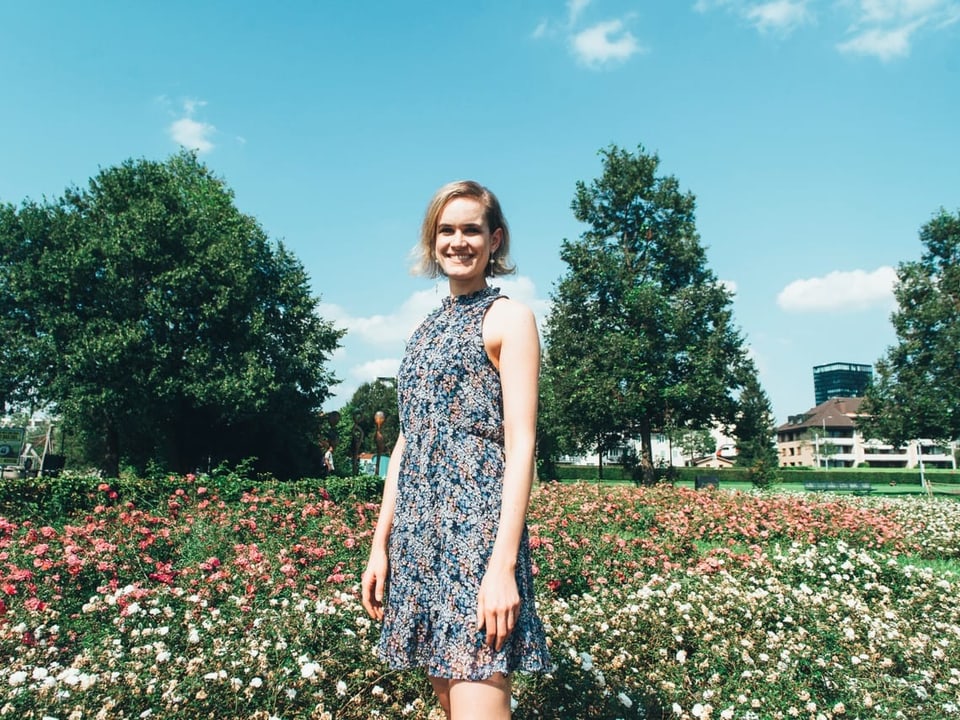 Eine Frau steht mit einem blumigen Sommerkleid inmitten einer blumigen Sommerwiese.