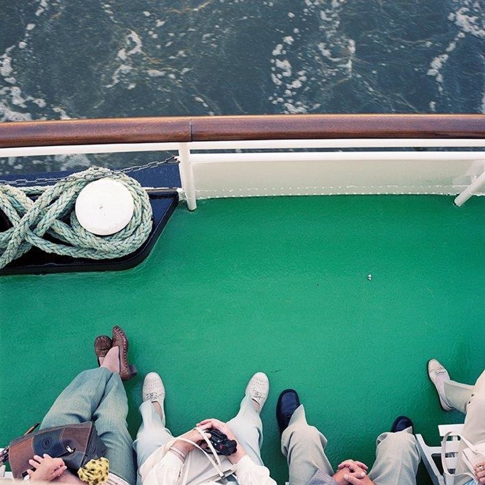 Ein paar Personen fahren auf einem Schiff auf dem Rhein. Man sieht ihre Füsse und das Wasser.