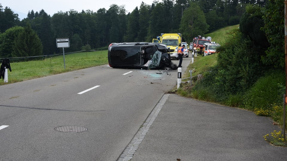 Ein schwarzes Auto liegt umgekippt auf der Strasse.