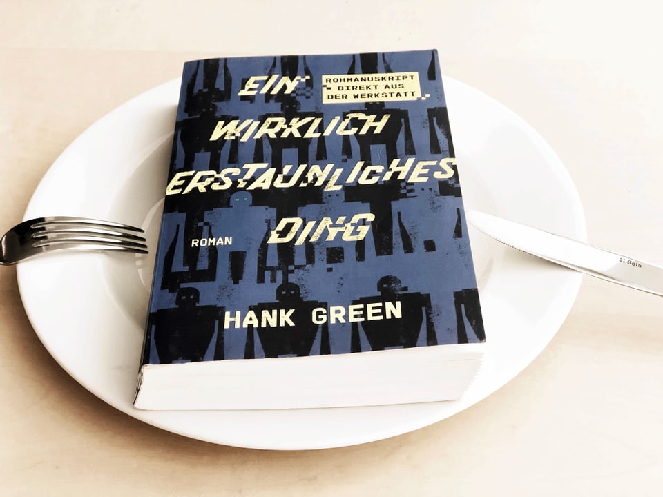 Der Roman «Ein wirklich erstaunliches Ding» von Hank Green liegt auf einem weissen Teller