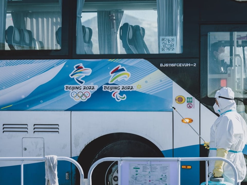 Ein Mann in Schutzanzug steht vor einem Olympia-Bus.