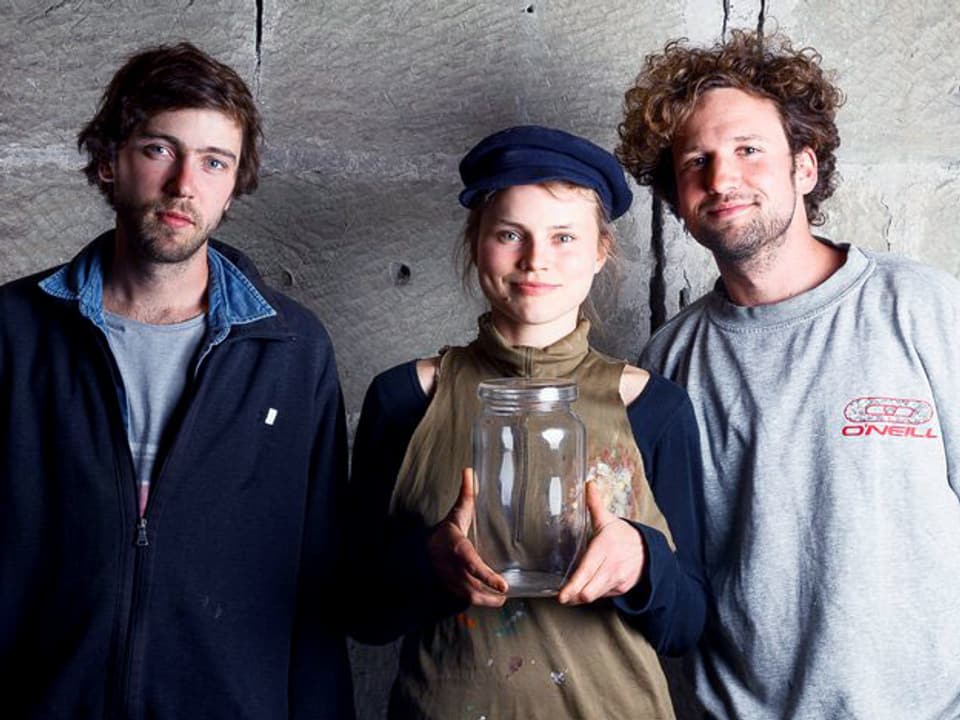 Proträt von zwei jungen Männern und einer jungen Frau. Die Frau in der Mitte, hält ein grosses Einmachglas in der Hand.