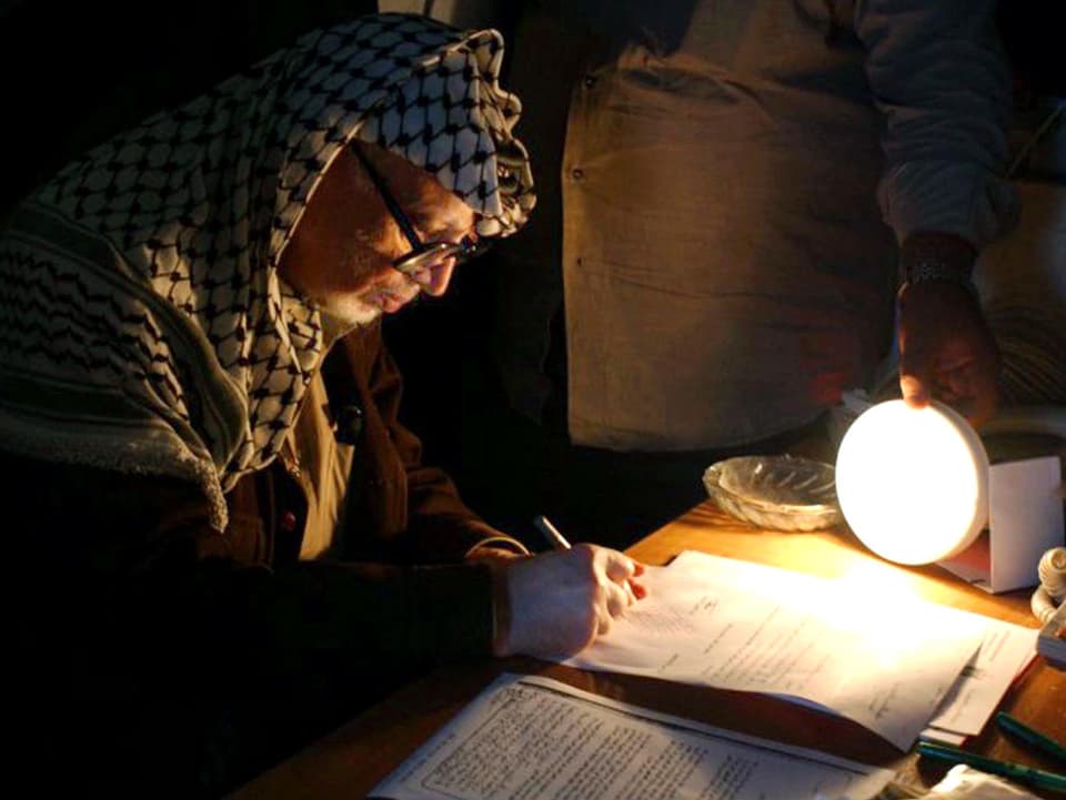 Arafat in einem Büro, das nur spärlich mit einer Lampe beleuchtet ist