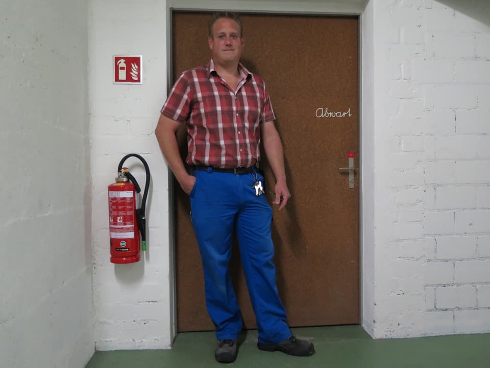 Martin Rufer steht vor einer Türe mit der Aufschrift «Abwart»