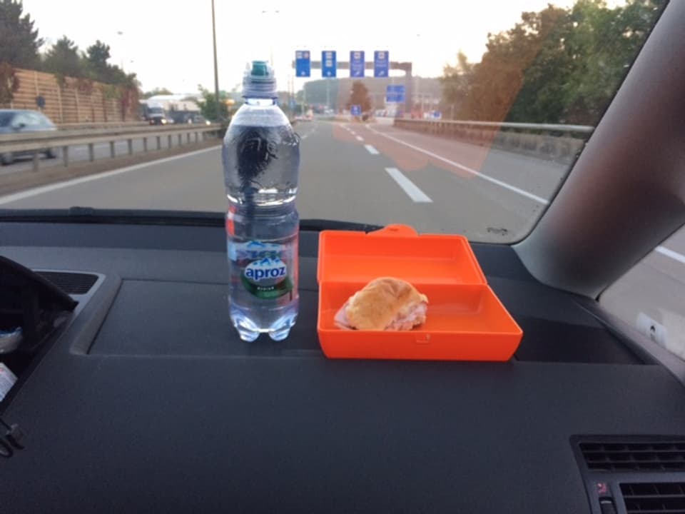 Mineralwasser und Lunchbox auf dem Armaturenbrett im Auto.
