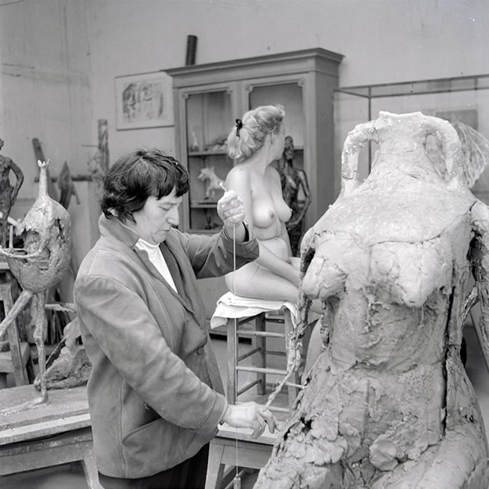Eine Frau macht eine menschliche Skulptur. Im Hintergrund ein weibliches Aktmodell.