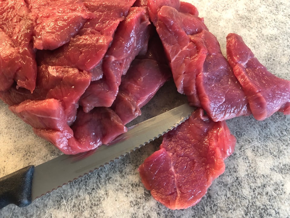 Rindfleisch wird mit einem Messer in kleine Stücke geschnitten. 