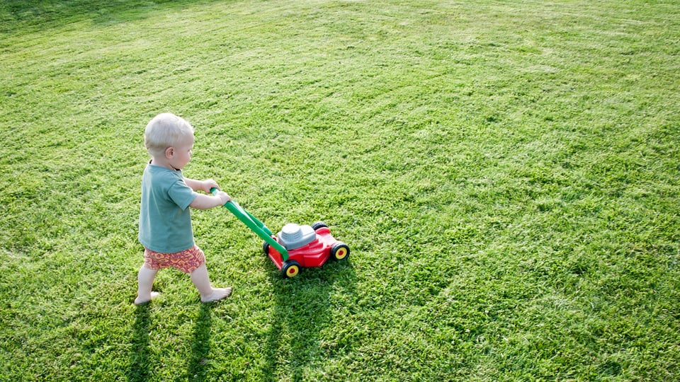 Ein Kind mäht den Rasen mit einem Spielzeugrasenmäher.