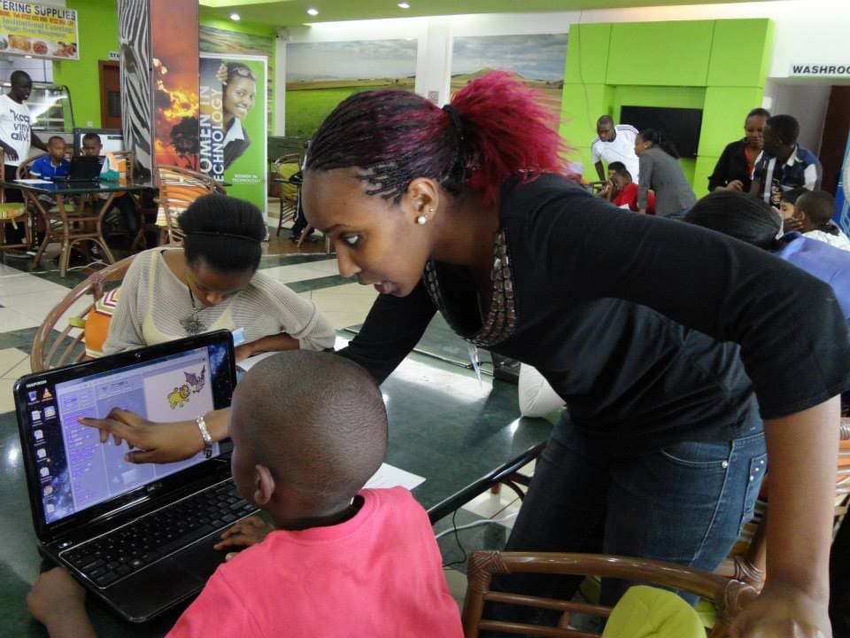 Eine Mitarbeiterin zeigt auf den Bildschirm eines Laptops, der vor einem Jungen steht.