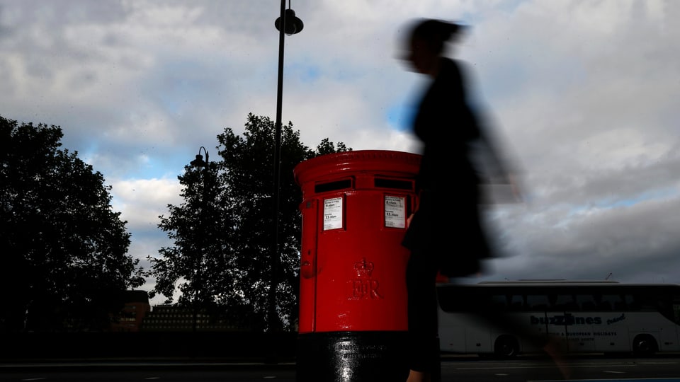 Eine Frau geht an einem roten Briefkasten in London vorbei.