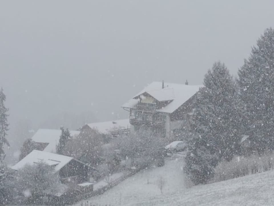 Es schneit an einem Hang, Häuser und Bäume