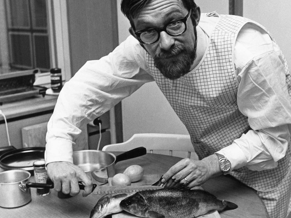 Ein Mann mit Bart und Brille bereitet in der Küche einen Fisch vor.