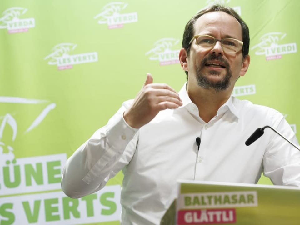 Mann mit hoher Stirn und Brille gestikuliert an einem Rednerpult, im Hintergrund das Logo der Grünen.