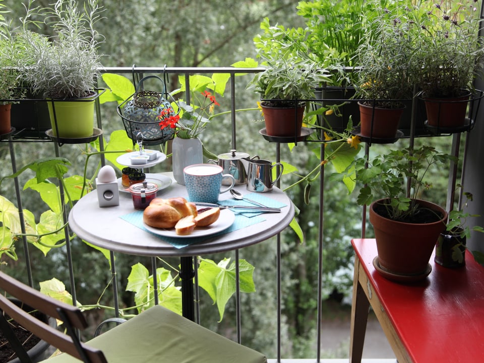 Tisch auf Balkon mit diversen Frühstücks-Utensilien. 