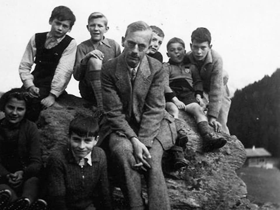 Mann und mehrere Kinder sitzen auf einem Felsen.