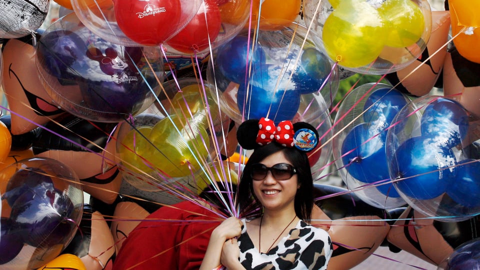 Junge Frau hält Ballone mit Aufschrift «Disneyland Hong Kong» in der Hand.