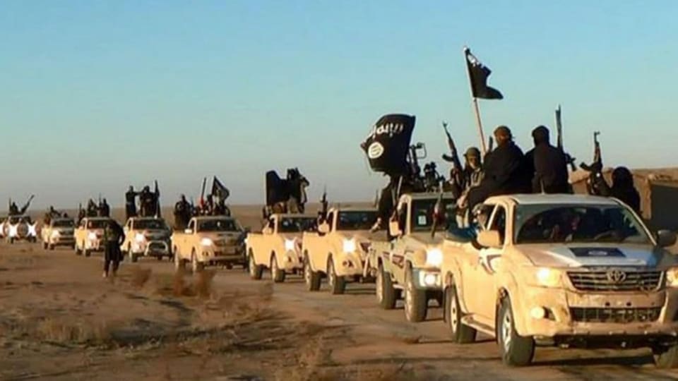 Ein Konvoi bestehend aus etwa 15 Autotransporter fahren über eine Landstrasse. Auf den Dächern sitzen bewaffnete des IS.