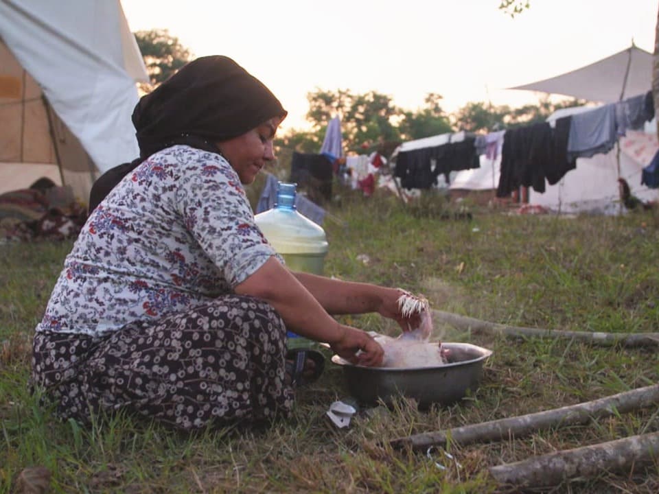 Eine Mutter kocht Abendessen auf dem Boden neben ihrem Zelt.