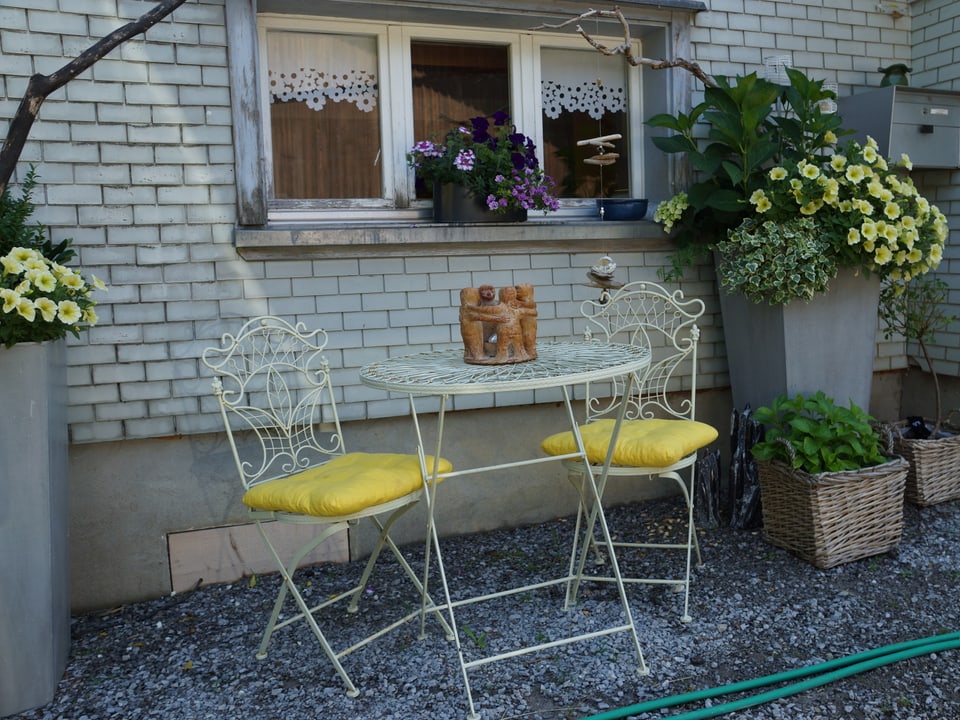 Ein Gartensitzplatz mit Tisch, zwei Stühlen und gelben Blumen.
